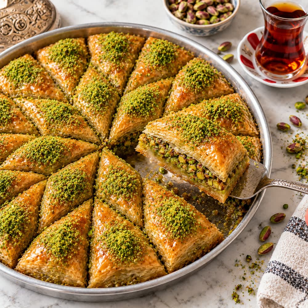 A tray of pistachio baklava with a glass of tea