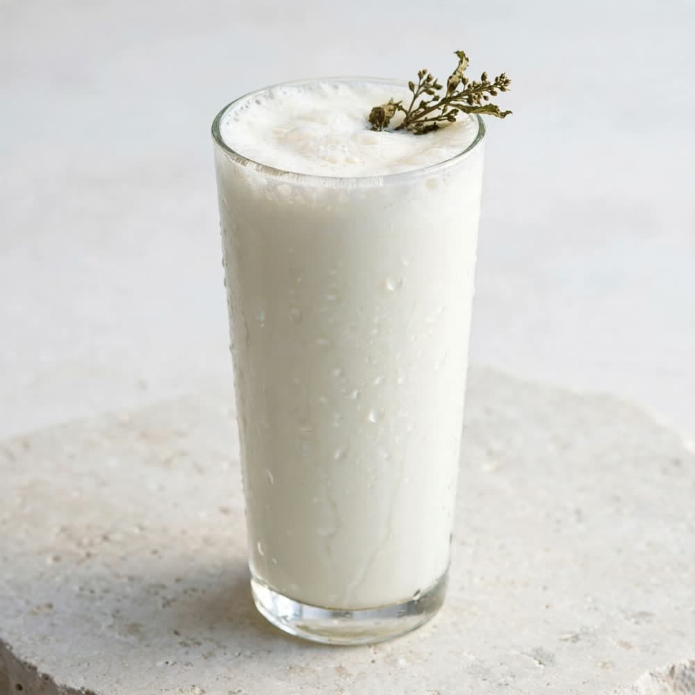 A tall glass of ayran with a frothy head and dried mint
